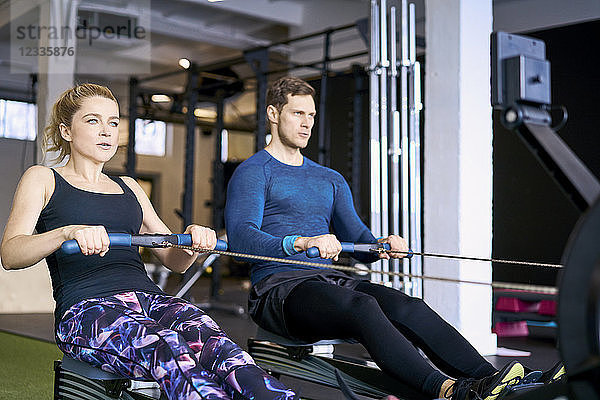 Man and woman at gym exercising together on rowing machines