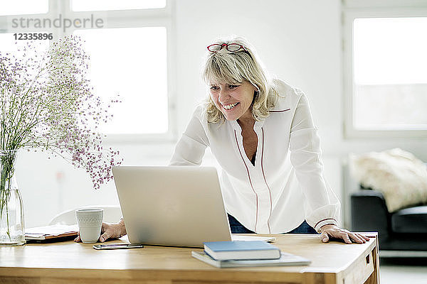 Smiling mature businesswoman working on laptop at desk