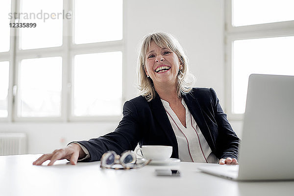 Portrait of laughing mature businesswoman with laptop at desk in the office