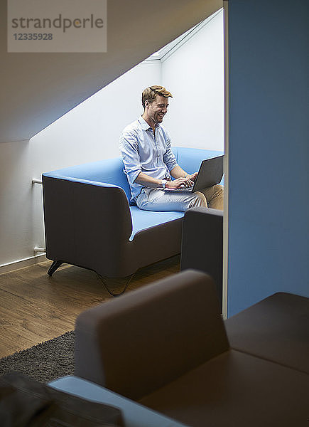 Laughing businessman sitting on couch working on laptop