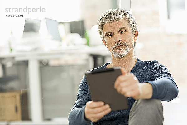 Mature man sitting in his office  using digital tablet