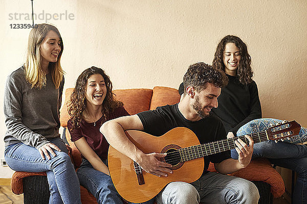 Happy freinds listening to man playing guitar on couch