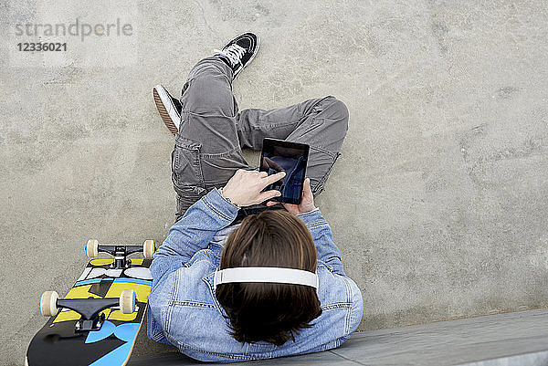 Young man with skateboard sitting on ground  using digital tablet