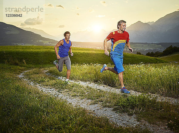 Two athletes running on field path at sunset