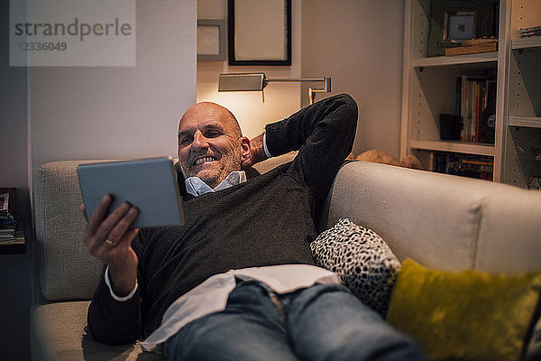 Senior man lying on couch  reading e-book