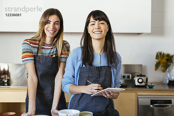 Portrait of two smiling women with notebook in kitchen