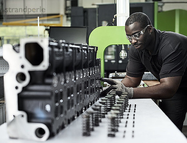Worker in metalworking factory loading cylinder head