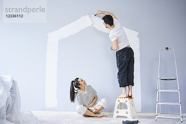 Couple painting house shape on wall in new apartment