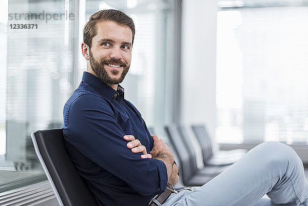 Smiling young businessman sitting in waiting area