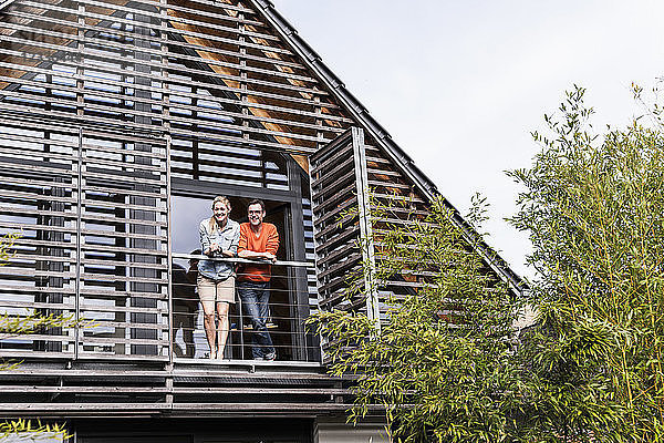 Smiling mature couple standing on balcony of their house