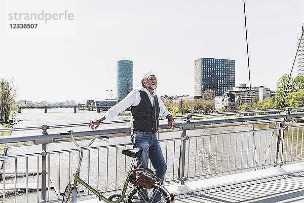 Mature man with bicycle listening to music on bridge in the city