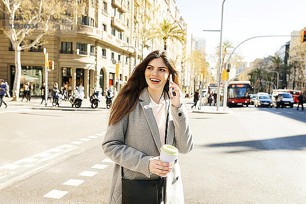 Spain  Barcelona  portrait of smiling young woman on the phone standing at roadside