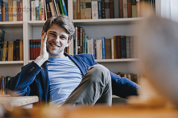 Portrait of smiling man sitting at bookshelf