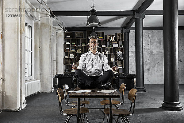 Portrait of mature businessman doing yoga on desk in loft office