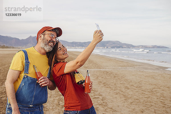 Couple with soft drinks taking selfie with smartphone on the beach