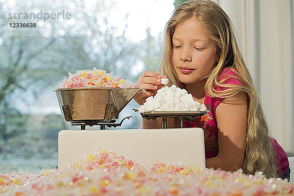 Girl behind scales  weighing sugar cubes and a lot of candies