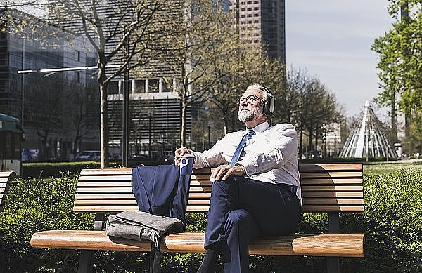 Mature businessman sitting on a bench listening to music