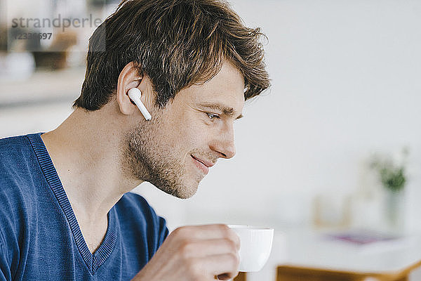 Smiling man in a cafe with earphone drinking coffee