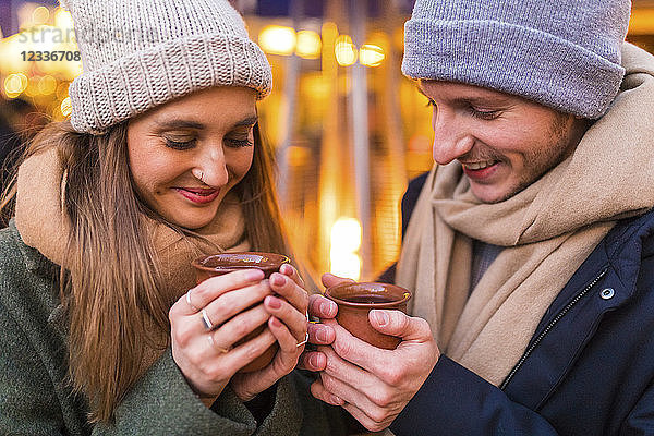 Happy young couple with cups of mulled wine at Christmas market