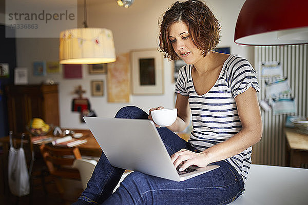 Portrait of mature woman sitting on kitchen table using laptop