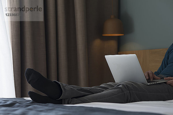 Young man lying on bed using laptop  partial view