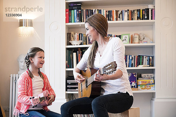 Mother and daughter playing guitar together at home