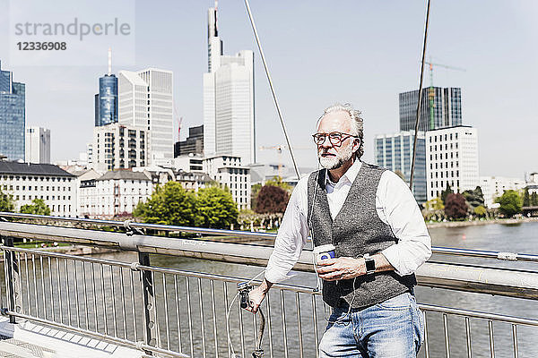 Mature man with bicycle and takeaway coffee on bridge in the city