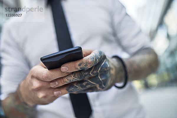 Young businessman with tattooed face using smartphone