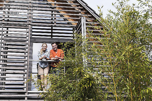 Smiling mature couple standing side by side on balcony of their house