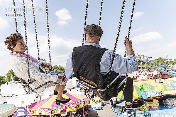 Senior couple hand in hand on chairoplane at funfair