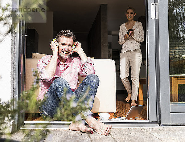 Happy man sitting at open terrace door listening music with headphones