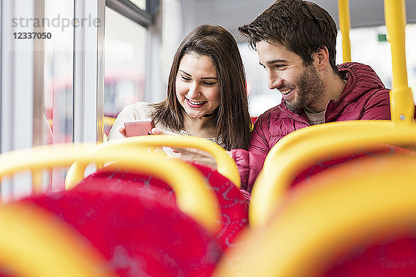 UK  London  happy young couple in bus looking at cell phone