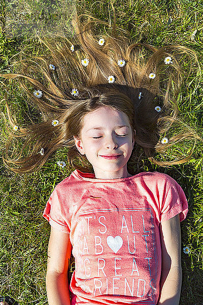 Portrait of smiling girl lying on grass in spring with daisies on hair