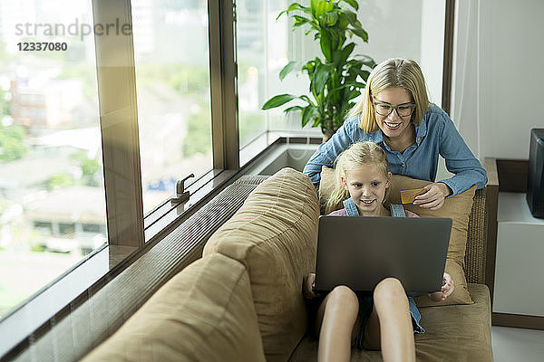 Mother and daughter in modern living room on a couch with laptop and credit card