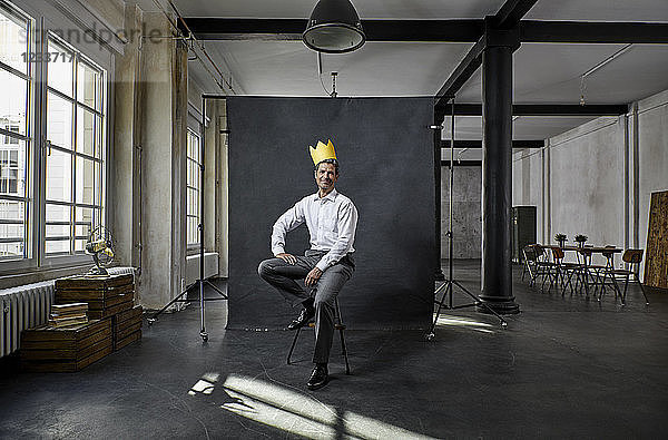 Portrait of mature businessman with crown in front of black backdrop in loft