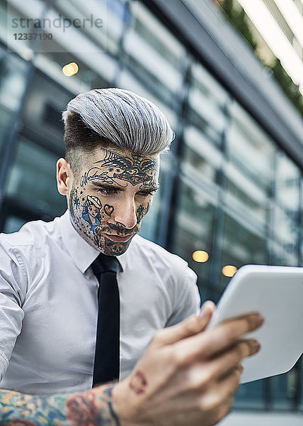 Young businessman with tattooed face  using digital tablet