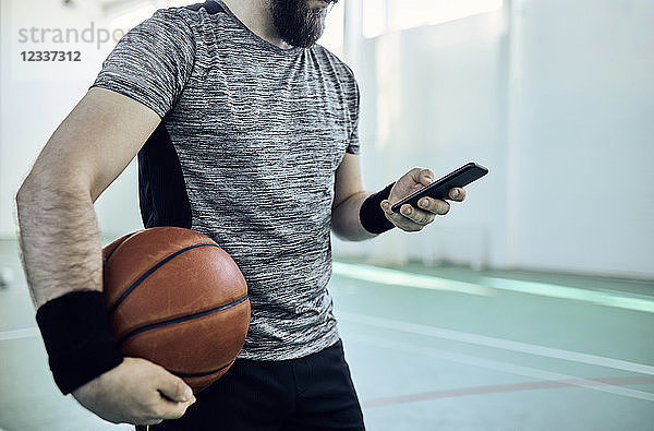 Man with basketball using smartphone  indoor