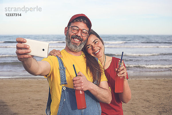 Couple with soft drinks taking selfie with smartphone on the beach