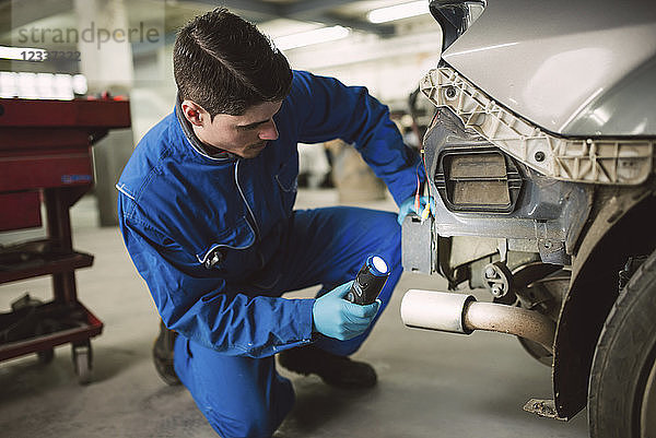Mechanic inspecting a car with a torch in a workshop