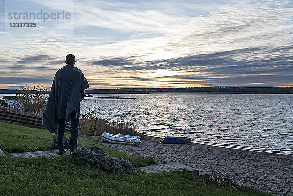 Man standing at lakeshore at sunset