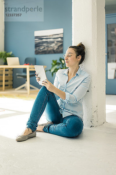 Young freelancer sitting on the floor in her studio using tablet