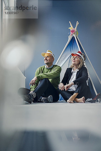 Smiling couple wearing sun visors sitting at teepee indoors