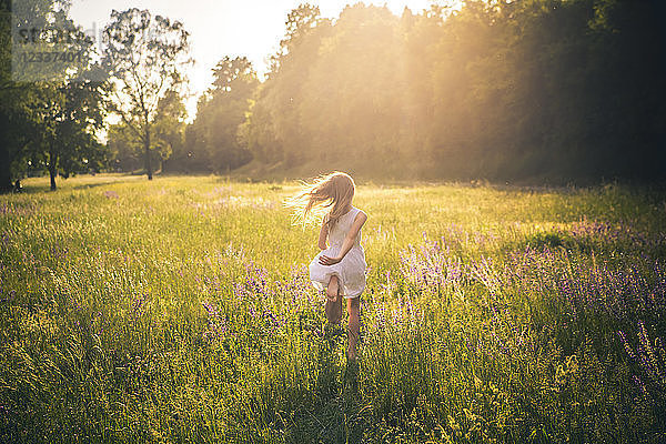 Back view of girl running on flower meadow at evening twilight