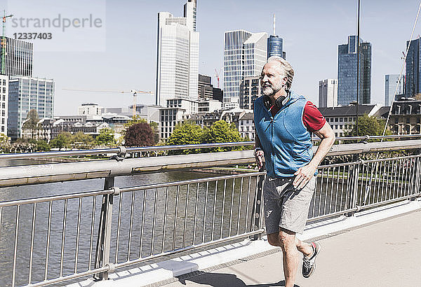 Smiling mature man with headphones running on bridge in the city