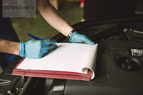 Close-up of mechanic taking notes on clipboard in his workshop