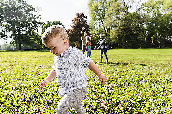 Boy walking in a park with family in background