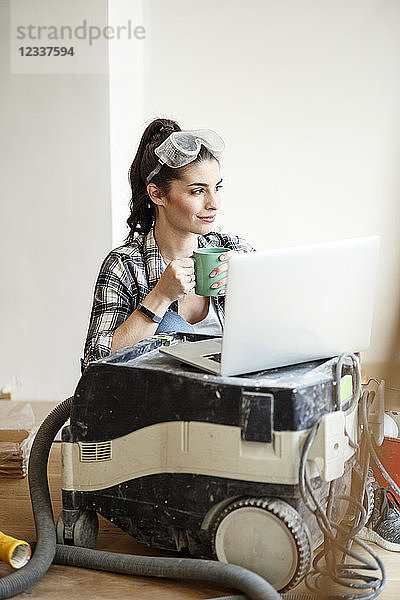 Young woman renovating her new flat  drinking coffee  looking at laptop