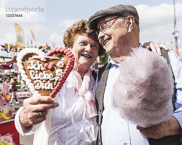 Portrait of happy senior couple with gingerbread heart and cotton candy on fair