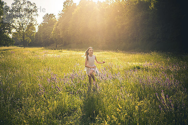 Smiling girl running on flower meadow at evening twilight