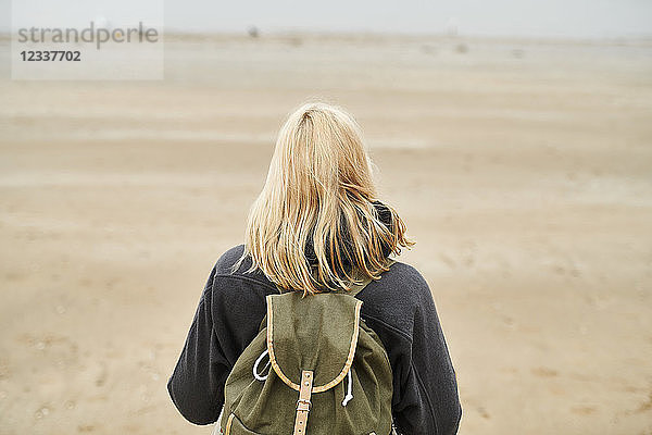 Back view of blond young woman with backpack on the beach